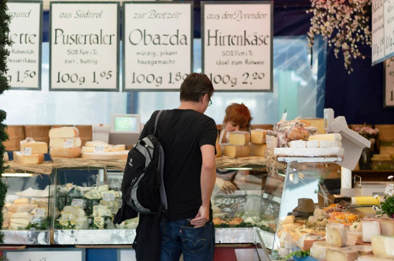 a man with a back pack looking at cheeses in a market