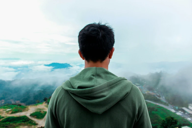 man in green jacket standing at the top of mountain