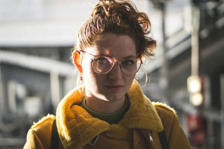 a woman in glasses and a coat is standing on the street