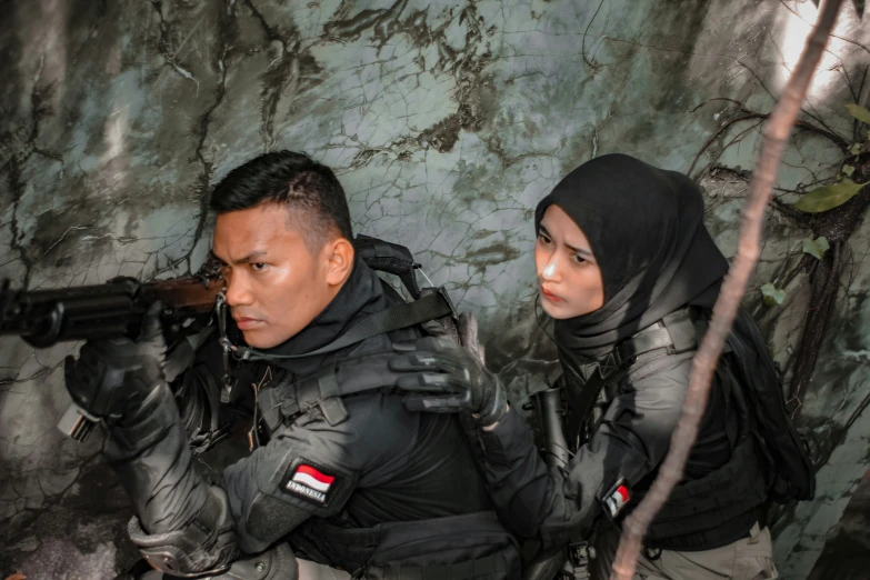 two people wearing gear holding guns against a stone wall