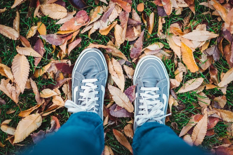 a man in blue jeans and white sneakers standing in the leaves