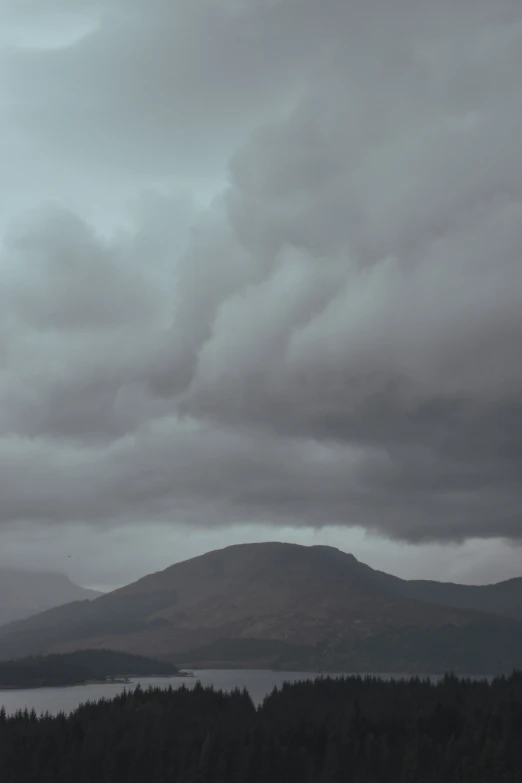 a cloudy sky with some trees and mountains in the distance