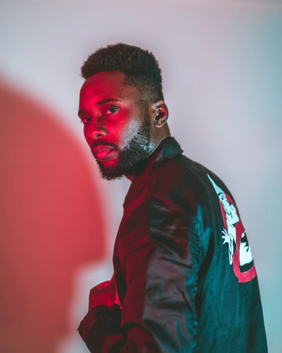 a young man in a leather jacket standing against a wall