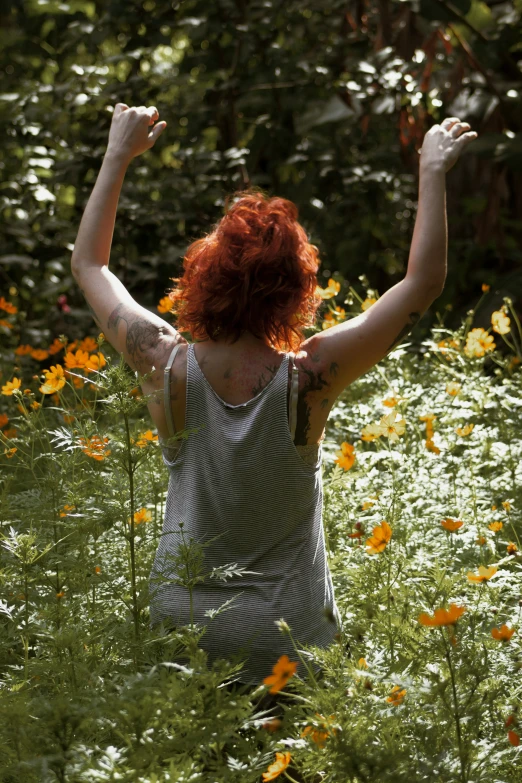 a woman in a field with flowers looking up and arms up