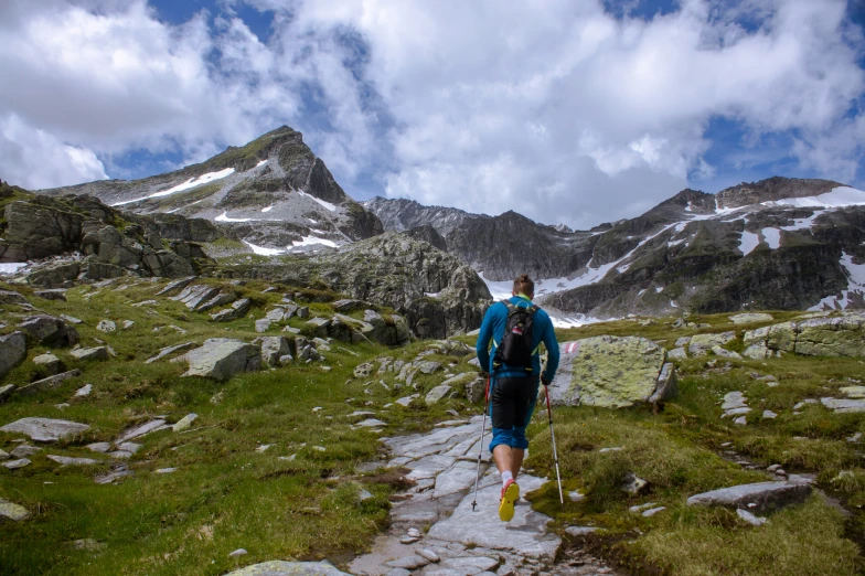 man in blue jacket walking on path near mountain