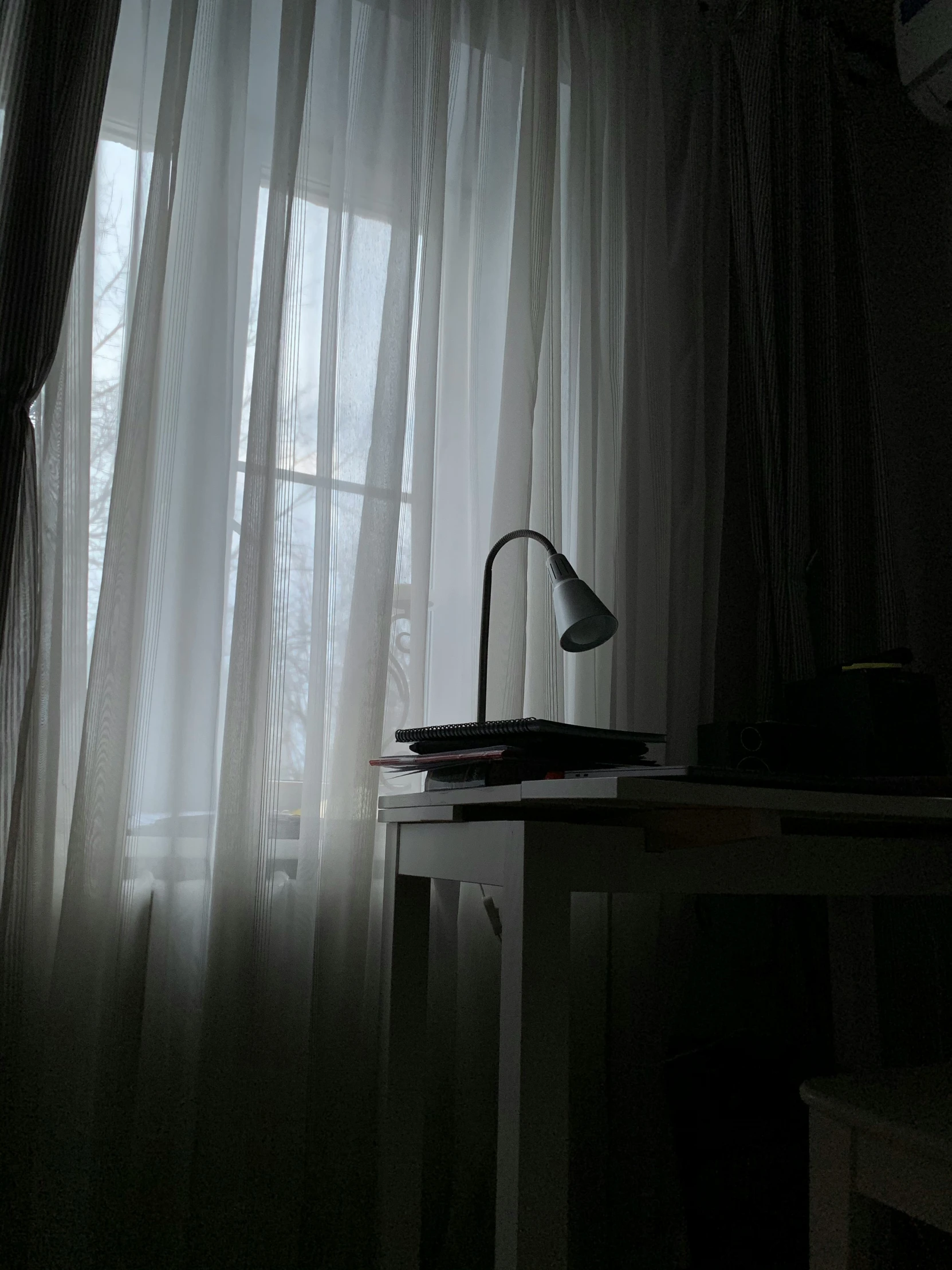 a computer desk and lamp in front of a window with sheer curtains