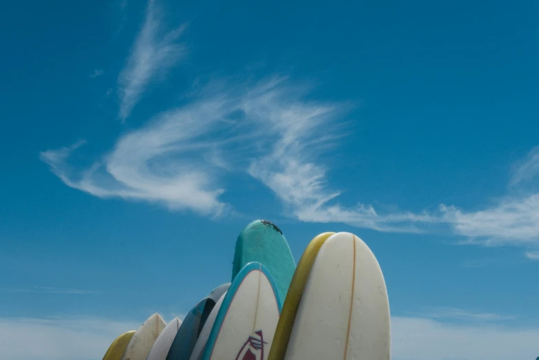 several surfboards stand in the sand under a cloudy blue sky