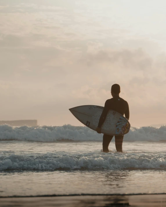 a person holding a surfboard while standing in the surf