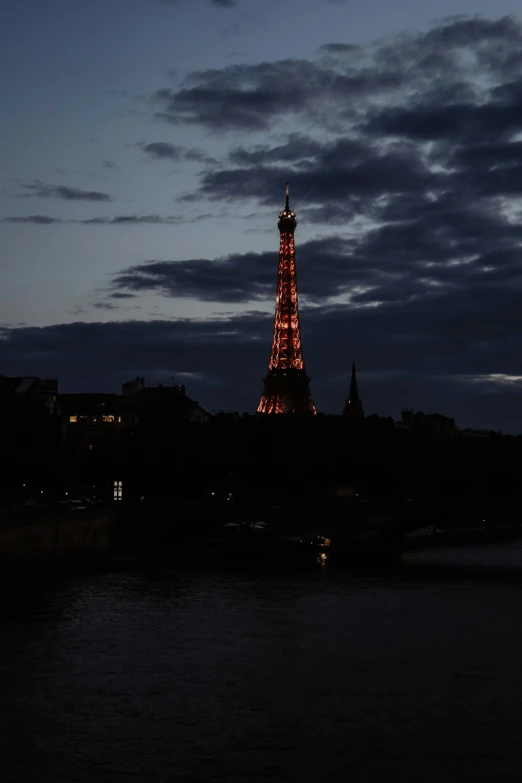 a large tower lit up in the evening, above the water