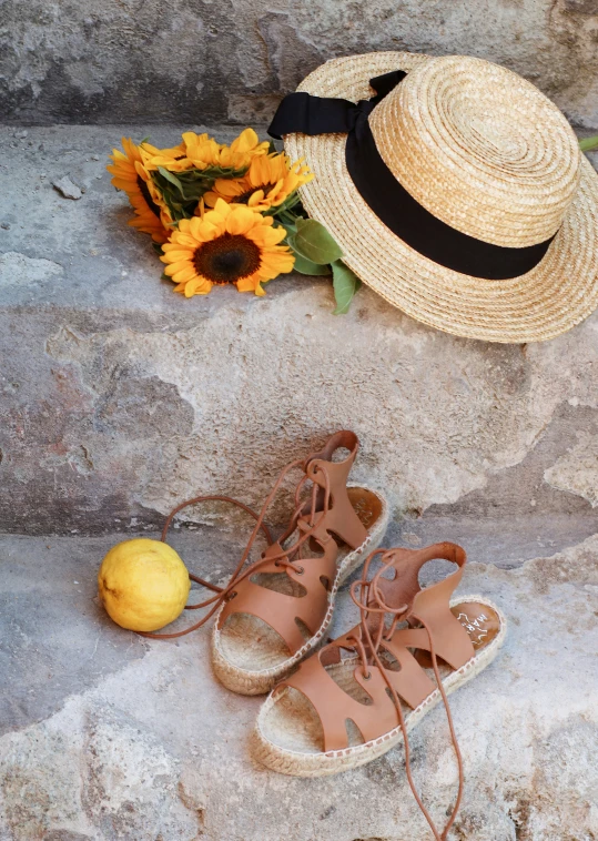 a straw hat, sunflowers and sandals on some stone