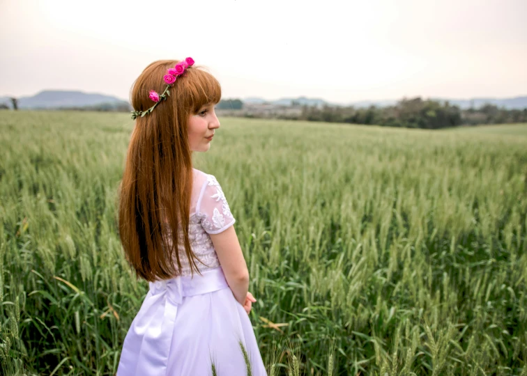 a girl in white dress looking up while standing in green field