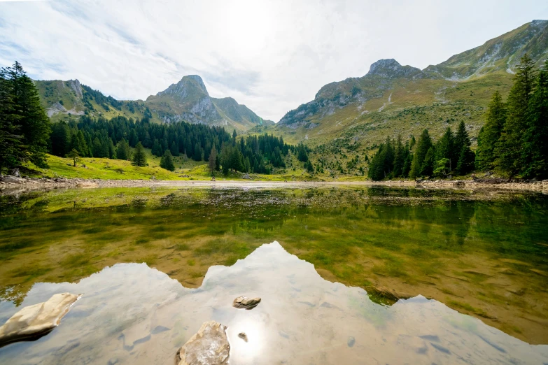 a lake in the middle of a forest with hills and pine trees around it