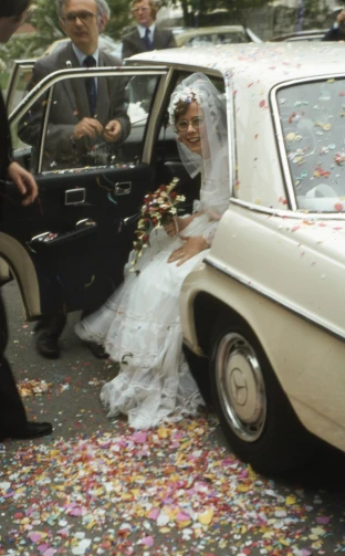 bride getting out of vintage car as groom walks in the doorway