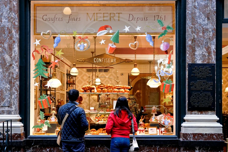 two people look at a display in the window of a pastry shop