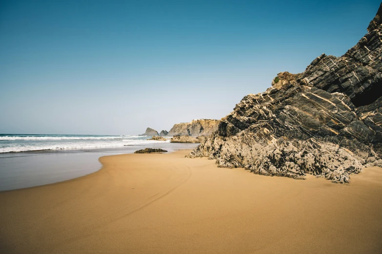 a sandy beach near a rock cliff on the water