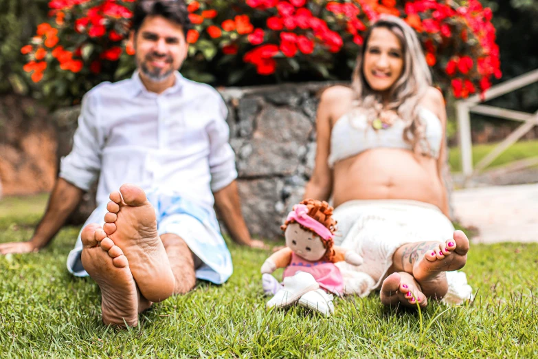 a pregnant woman with a baby doll sitting in a grassy area next to two other people