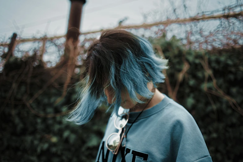 a man with long hair and piercing in front of bushes