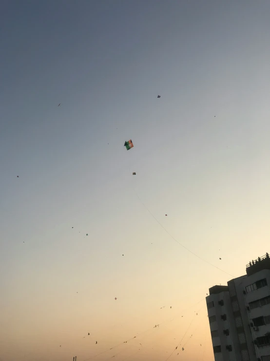 multiple kites flying high up in the sky above some buildings