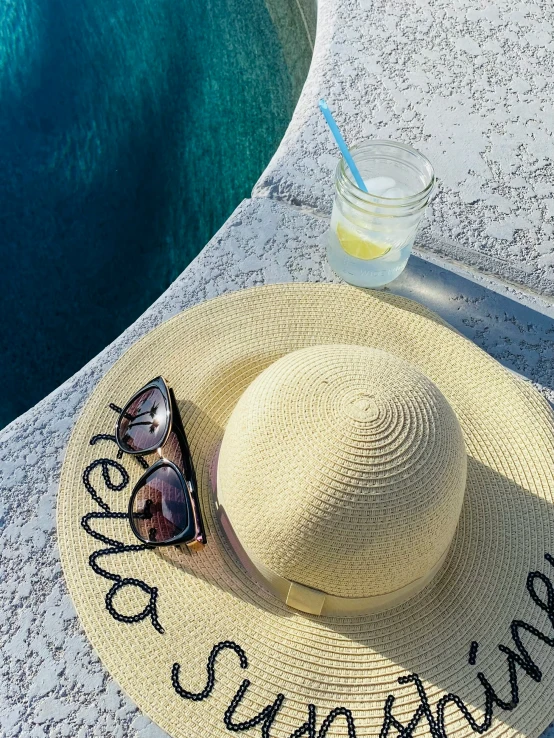 a hat, sunglasses, and bottle sitting on a mat next to a pool