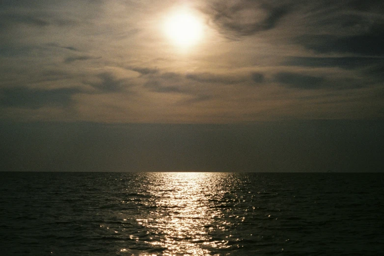 sun shining behind clouds over the ocean