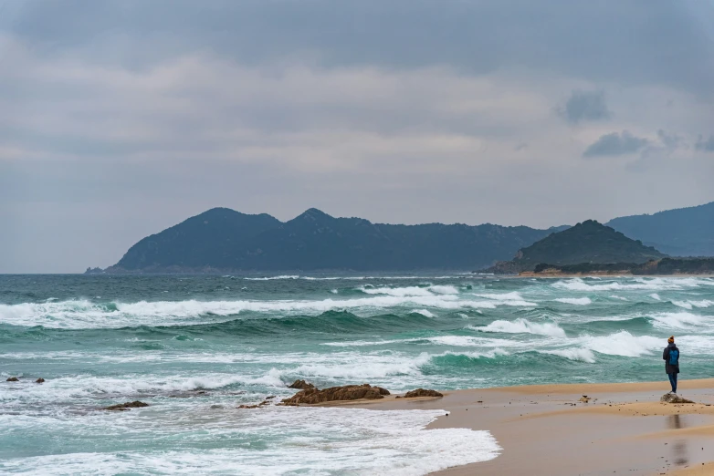 two people walking along the edge of a wave filled beach