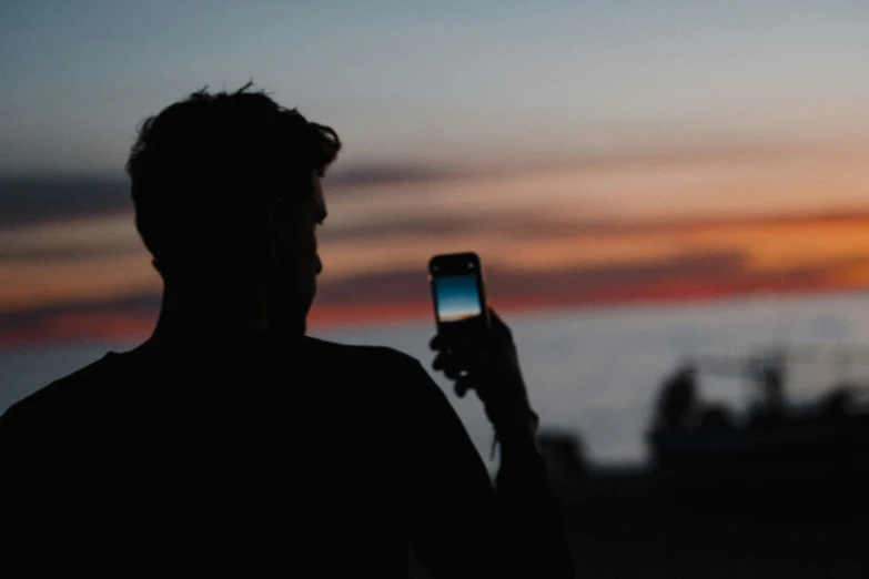 silhouette of man using cell phone outdoors at sunset