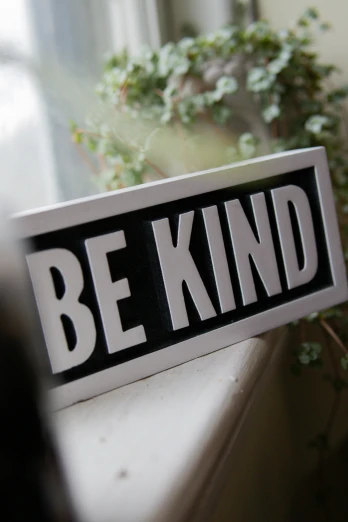 a sign that says be kind is displayed on a windowsill