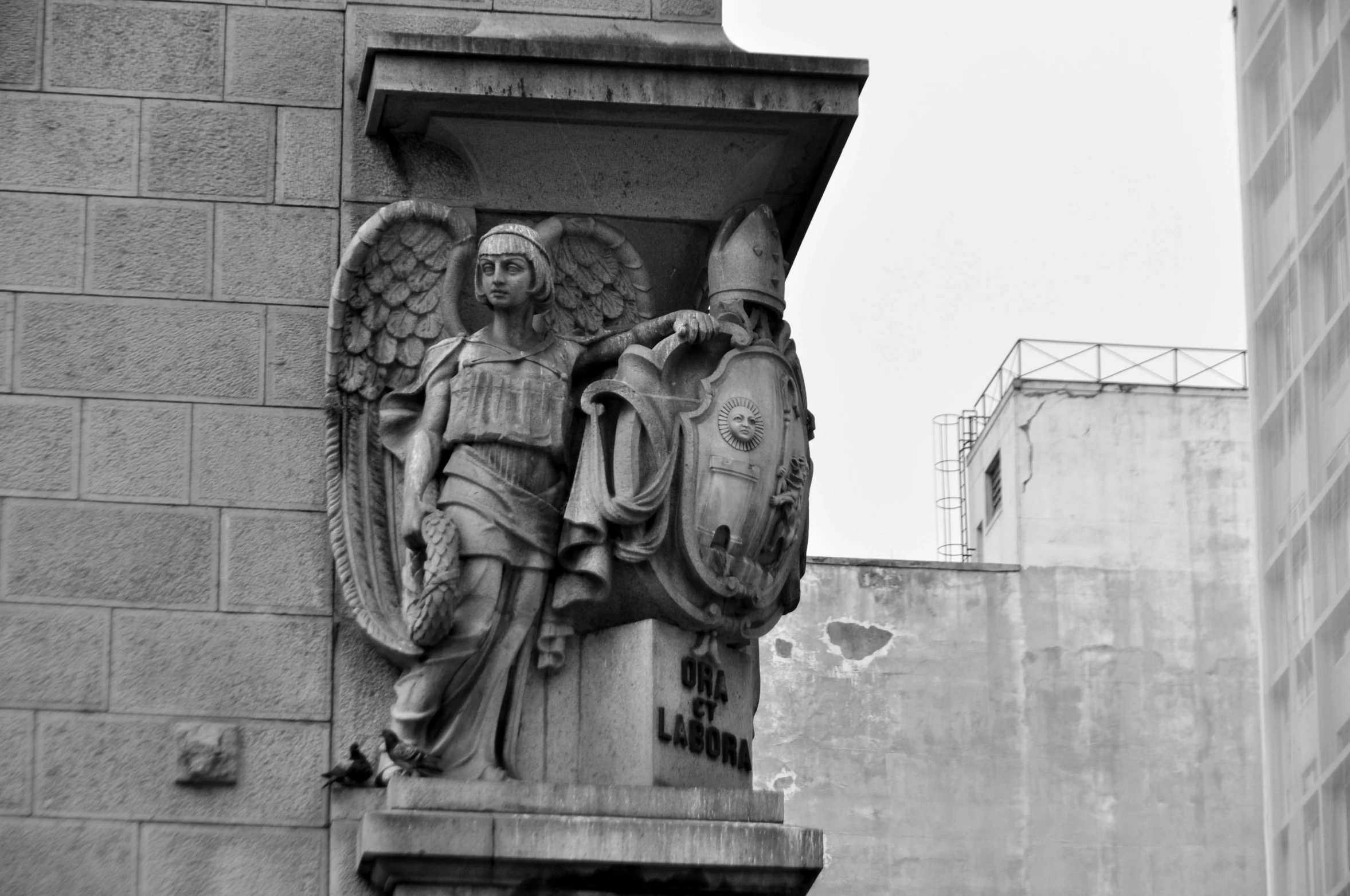 a stone gargoyle with two wings stands next to an urban building