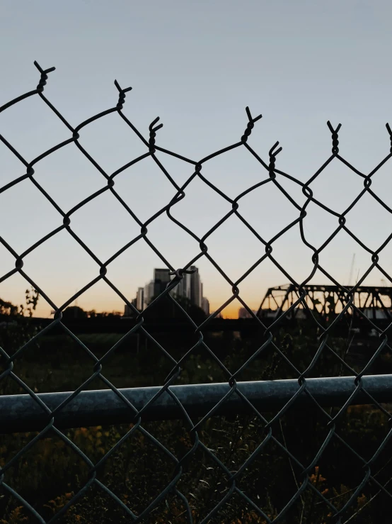 this is a view through a chain link fence, with a train bridge in the distance