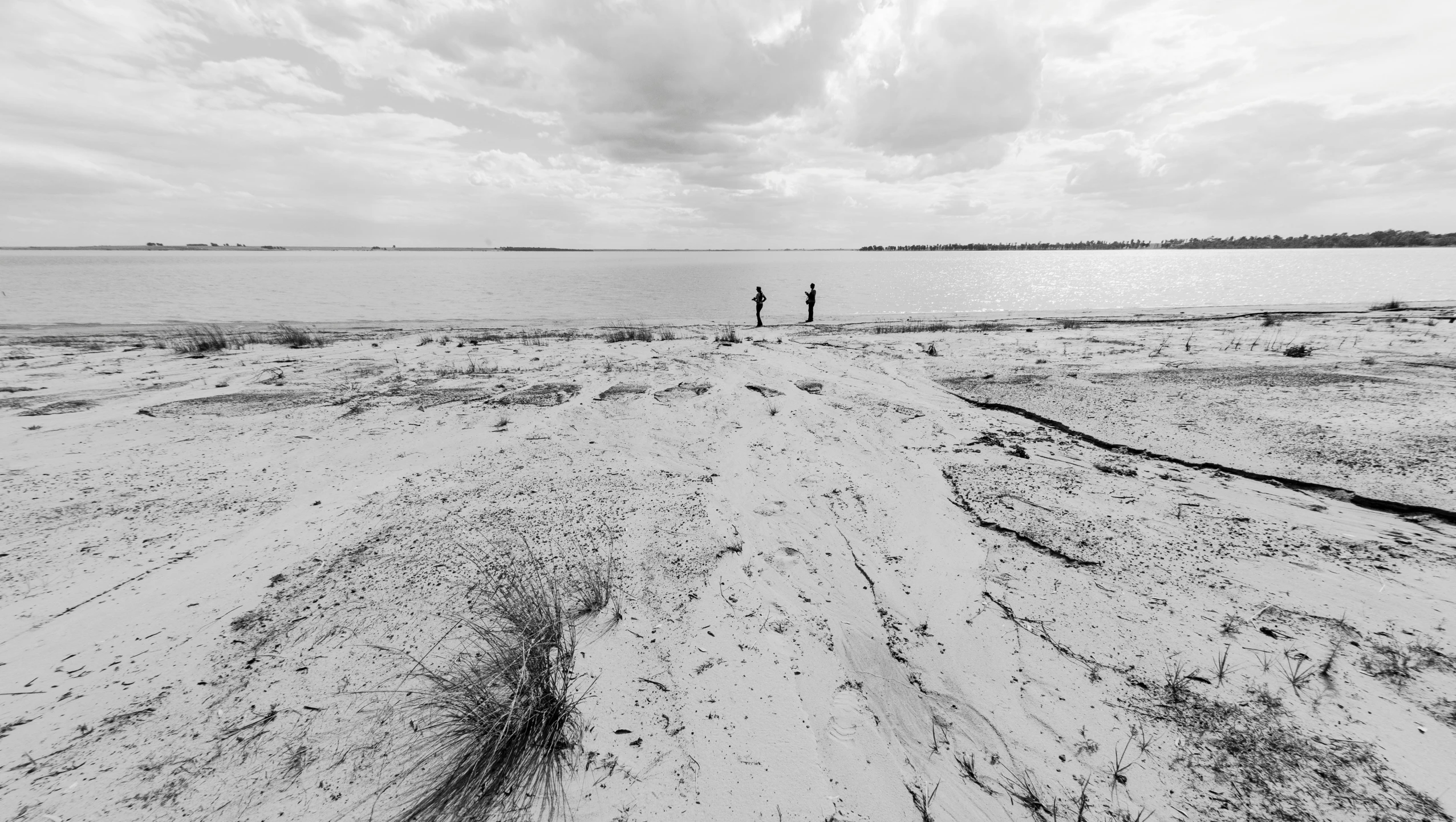 two people walk along the beach with water in the background