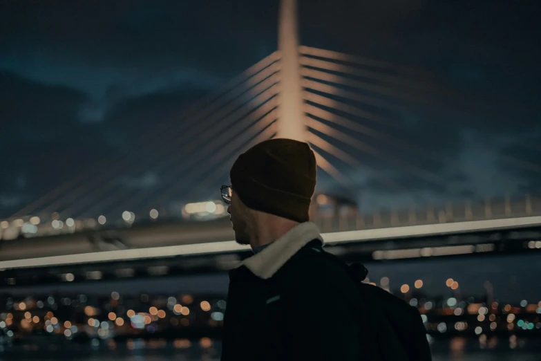 a man with a hat and glasses looks up at a bridge in the distance