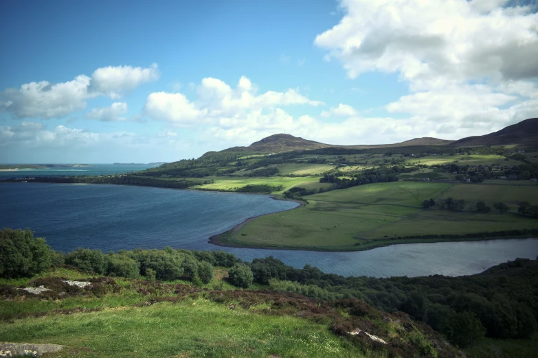 a landscape with water, trees, and hills on a sunny day