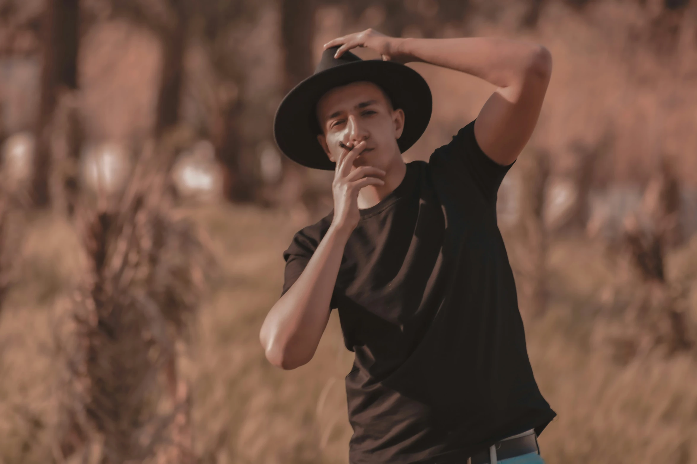 a young man wearing a black hat in front of trees