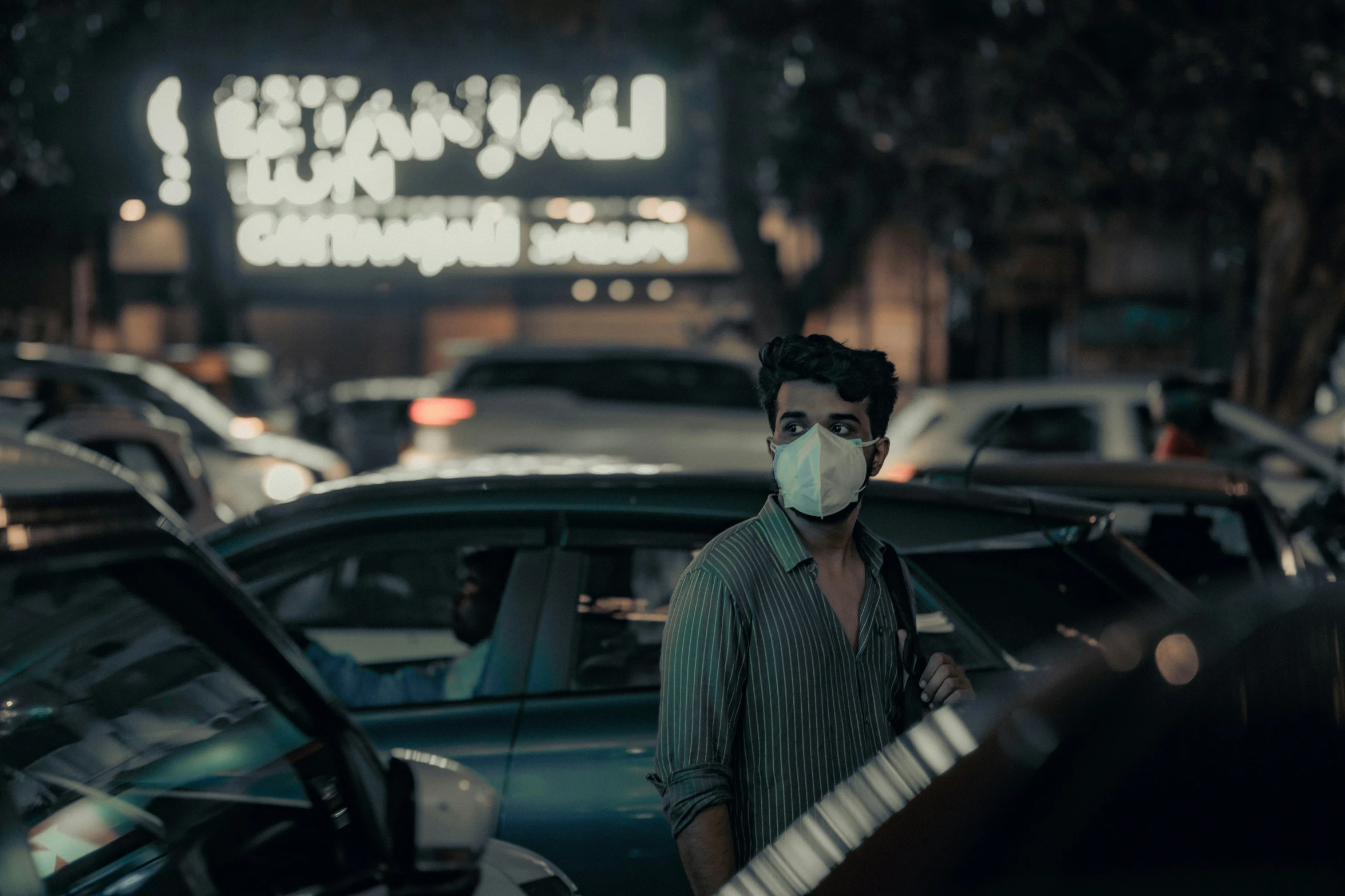 a person wearing a face mask next to parked cars