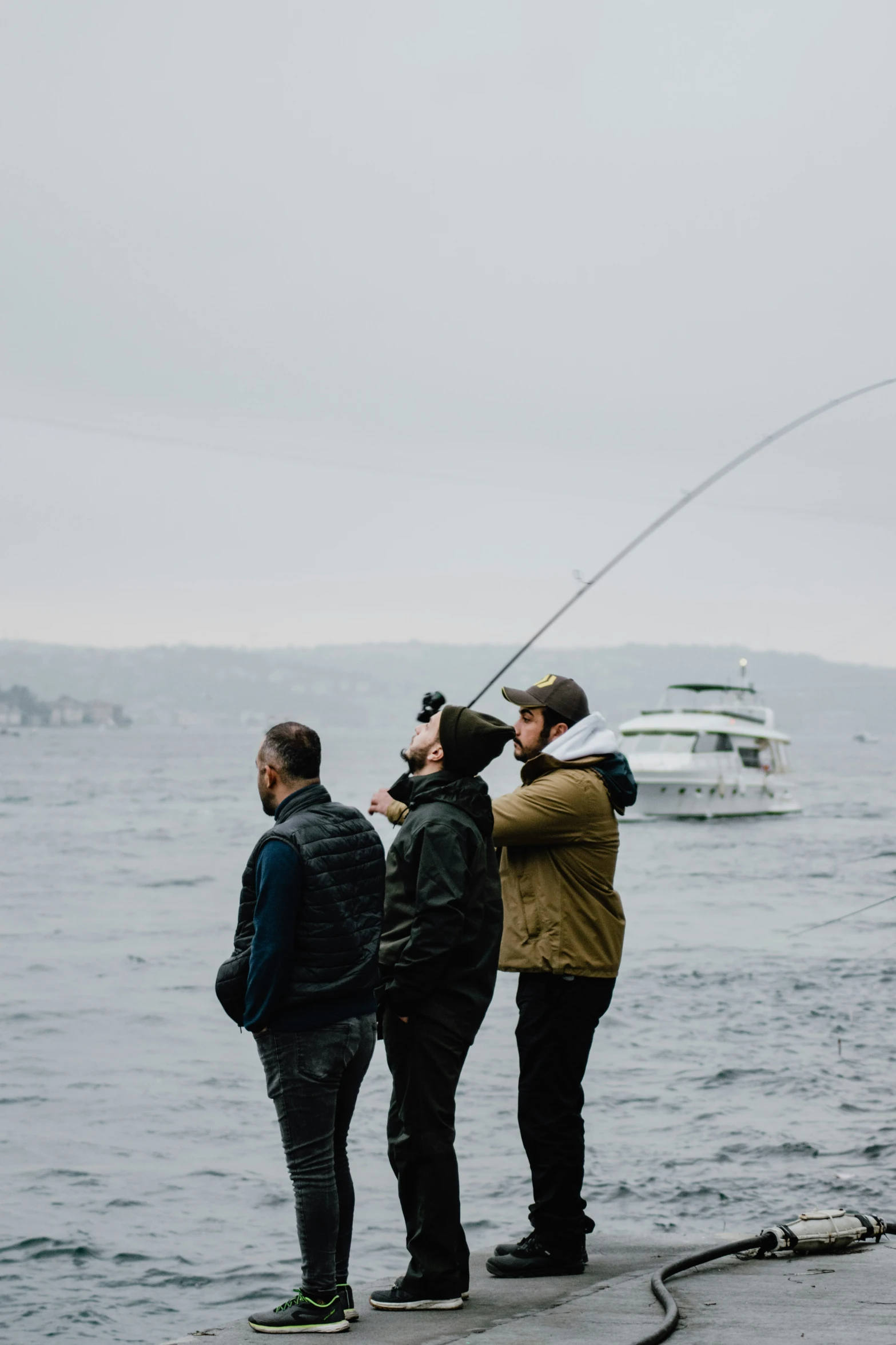 three men fishing in the ocean with boats in the background