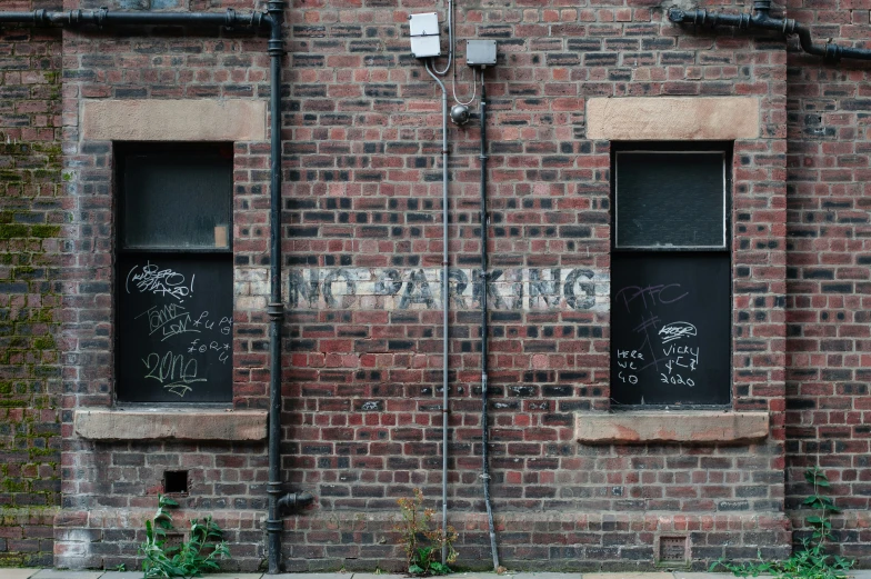 two windows in a brick wall with graffiti on the side