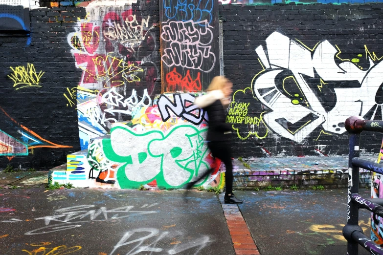 a woman walks through the city next to a graffiti wall