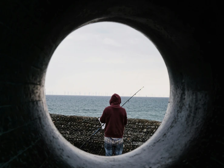 a man holding a fishing rod standing in front of the ocean