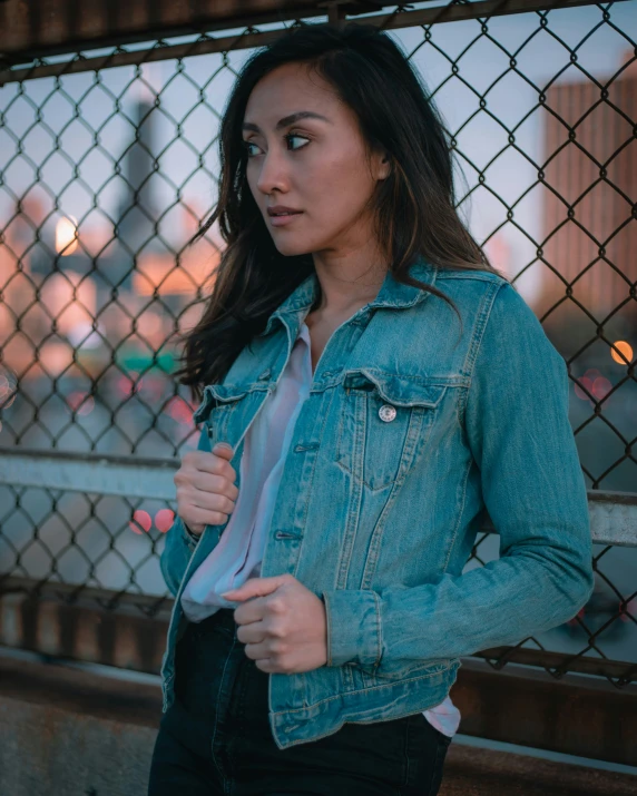 a girl in a blue jacket standing next to a chain link fence