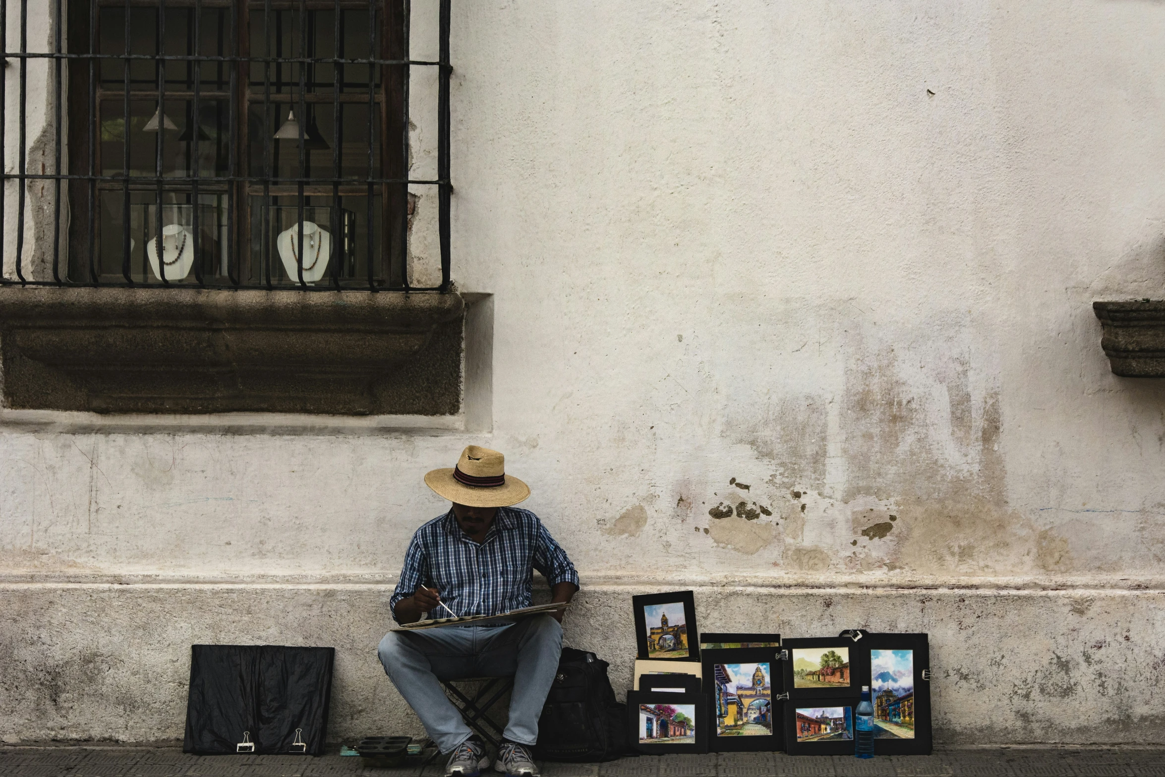 a man sitting on a sidewalk next to an outdoor wall