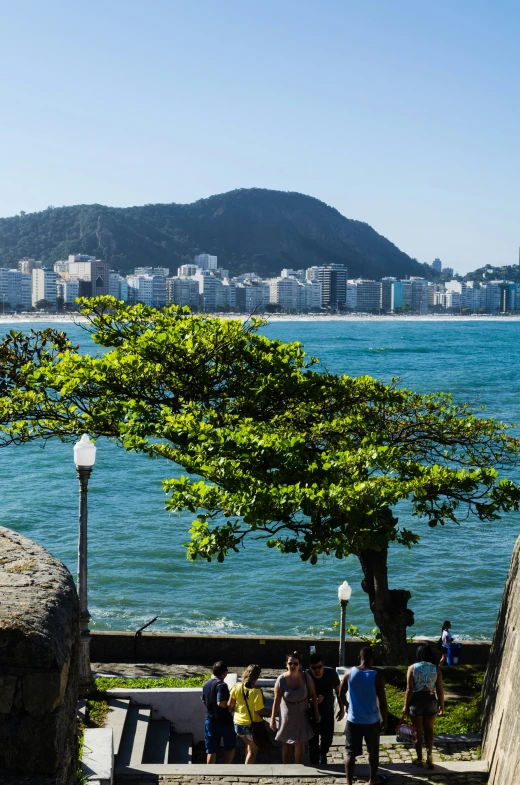 people walking up steps near the beach, and in the distance is a body of water with the city in the background