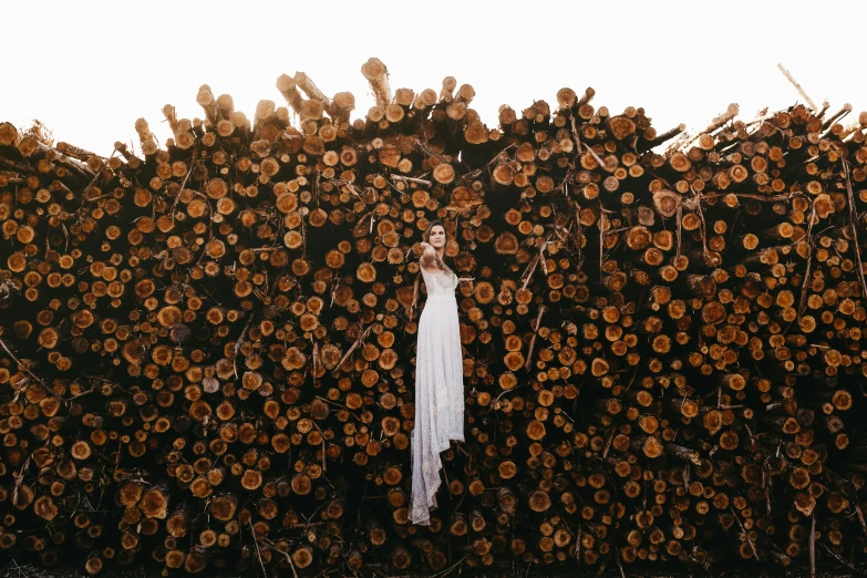 woman in white dress standing between stacks of logs