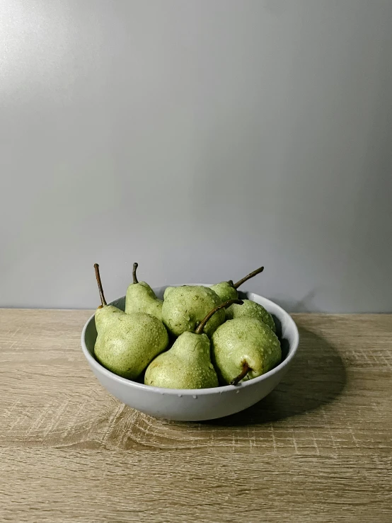 some pears are in a white bowl on a table