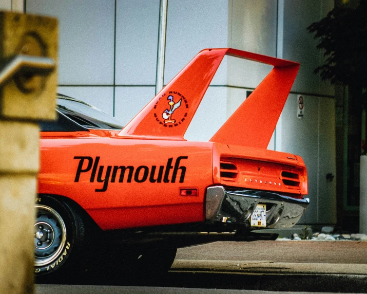 an orange plymouth sits parked next to another car