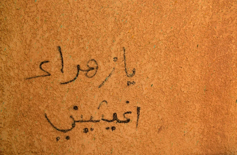 writing in arabic and english written on an orange wall