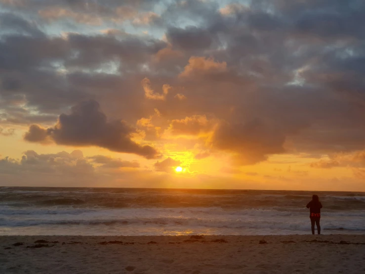 a man is standing on the beach at sunset