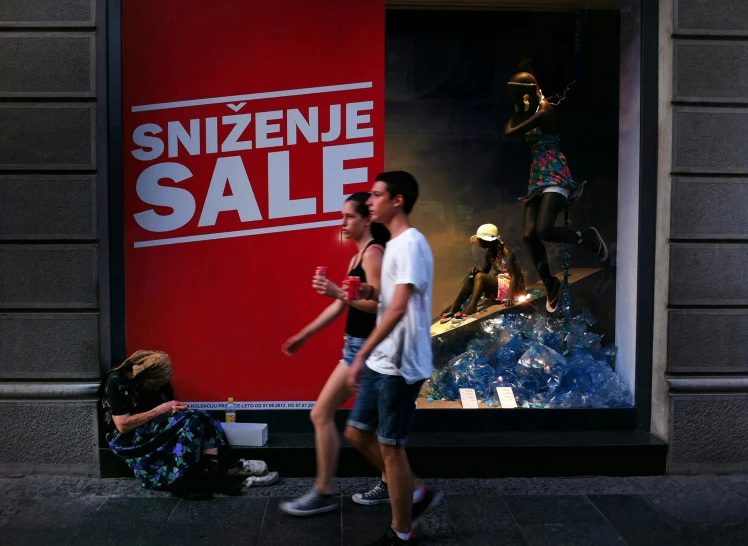 a man and woman walking past a display window with an ad for snezenue sale