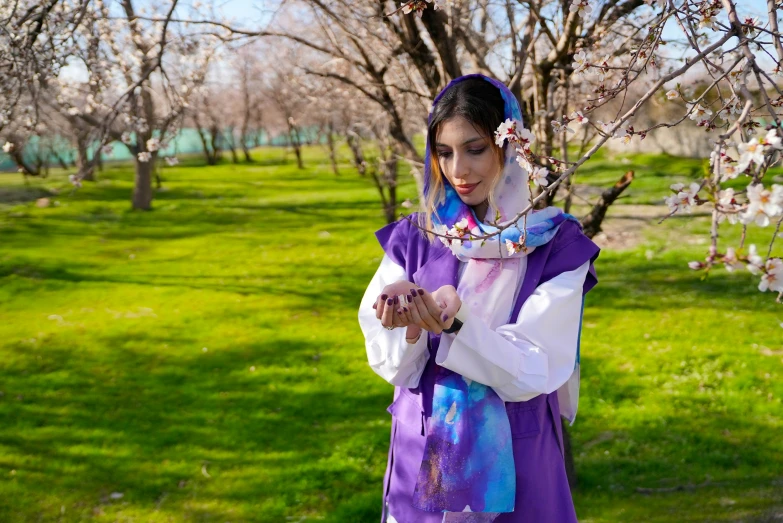 a woman in purple poses on the grass next to a tree with many blossoming trees