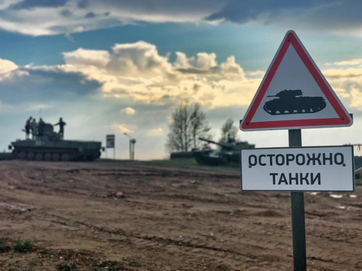 a road sign next to the dirt with a tank in the background