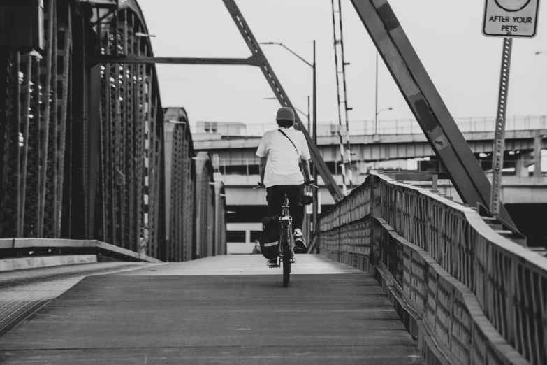 black and white pograph of a man riding a bicycle across a bridge